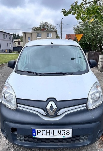 Biały samochód dostawczy Renault z tablicą rejestracyjną PCH LM38, zaparkowany na zewnątrz, z widocznymi budynkami, drzewami i znakiem drogowym w tle pod chmurnym niebem.