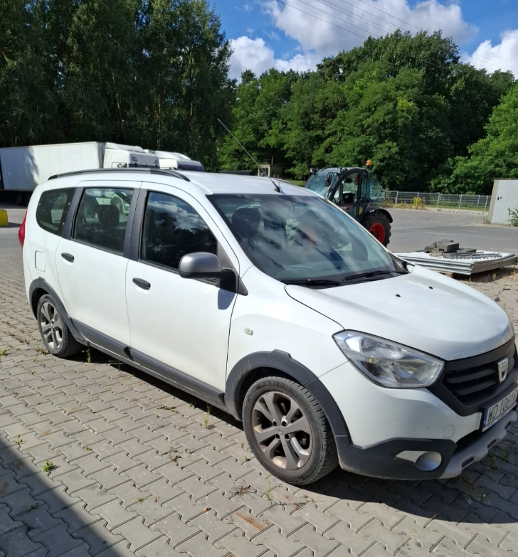 Biała Dacia Lodgy Stepway, kombivan z plastikowymi osłonami, zaparkowany na brukowanym placu.